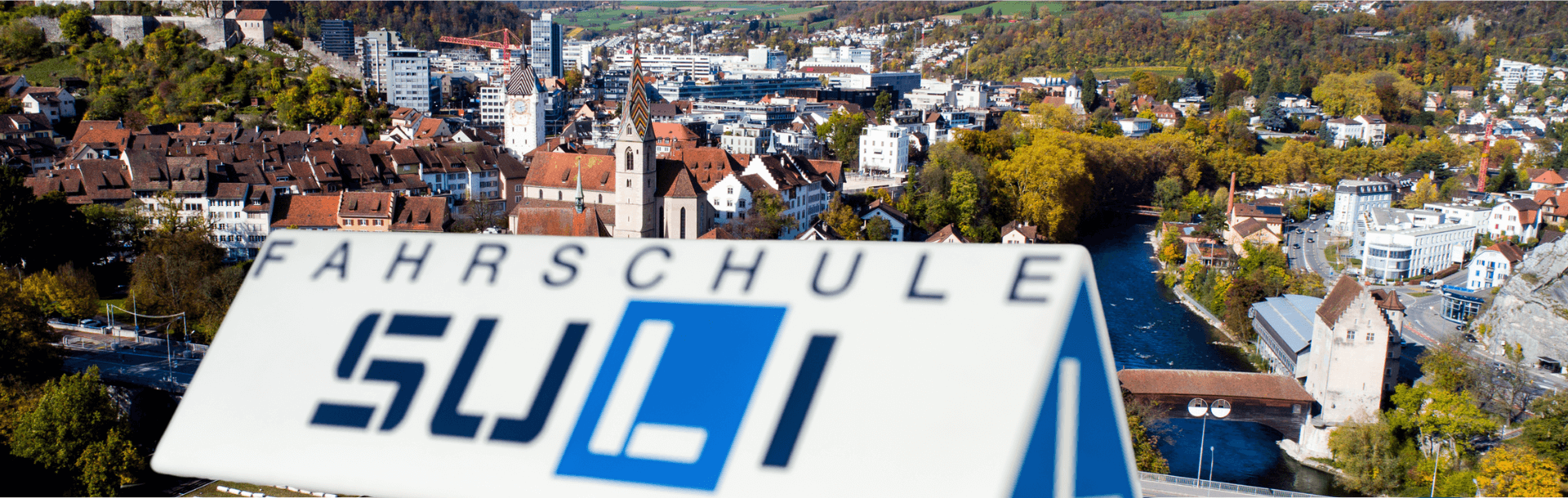 Ein modernes Fahrschulauto mit dem Logo der Fahrschule Suli steht vor einer städtischen Kulisse in Baden.