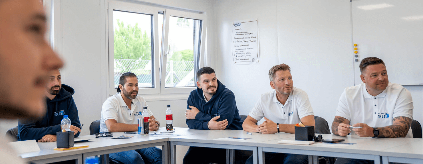 Teilnehmer beim Verkehrskundeunterricht, die aufmerksam den Erklärungen des Fahrlehrers folgen und Verkehrssituationen im Unterricht besprechen.