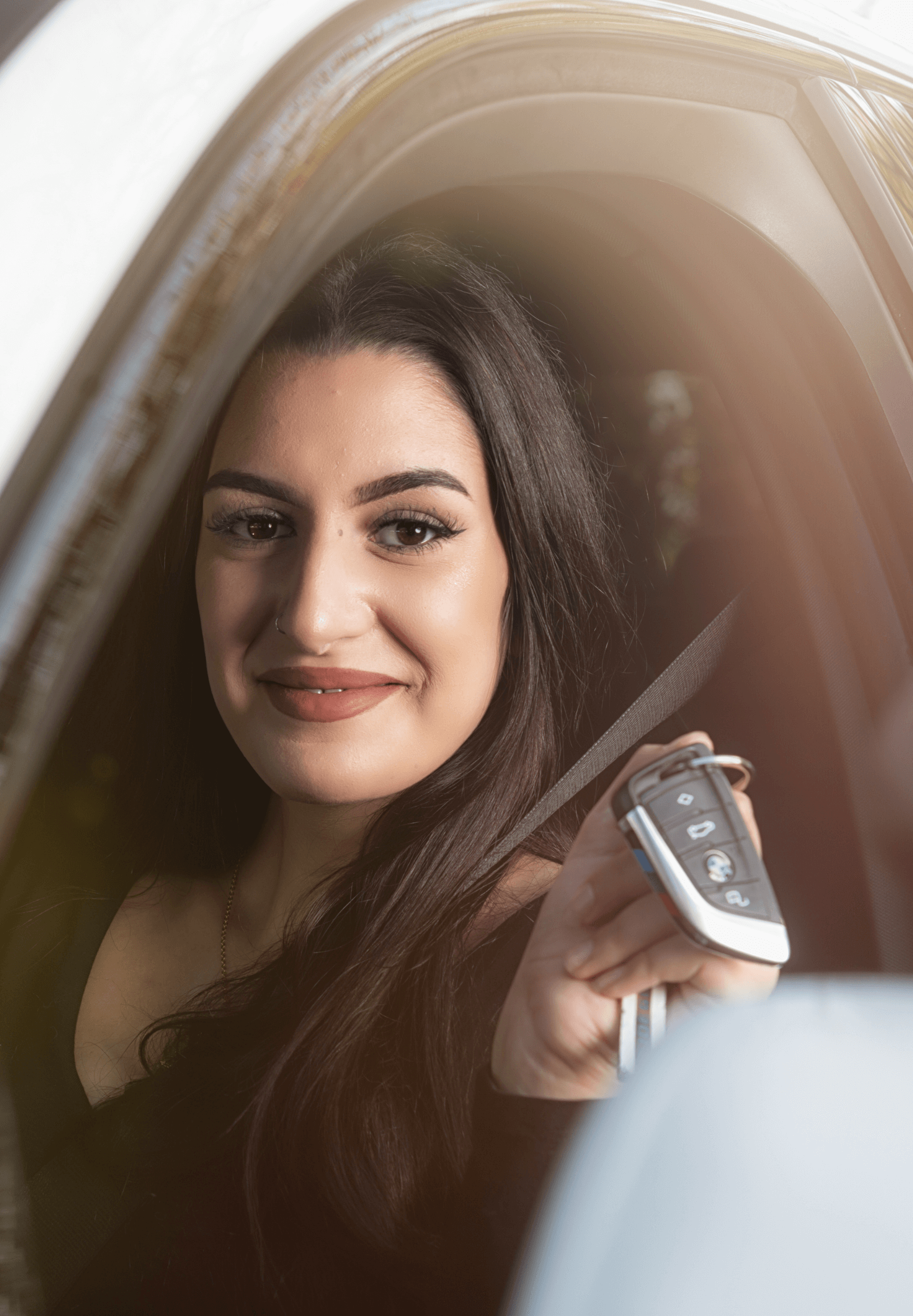 Junge Frau sitzt lächelnd im Auto nach bestandener Fahrprüfung.