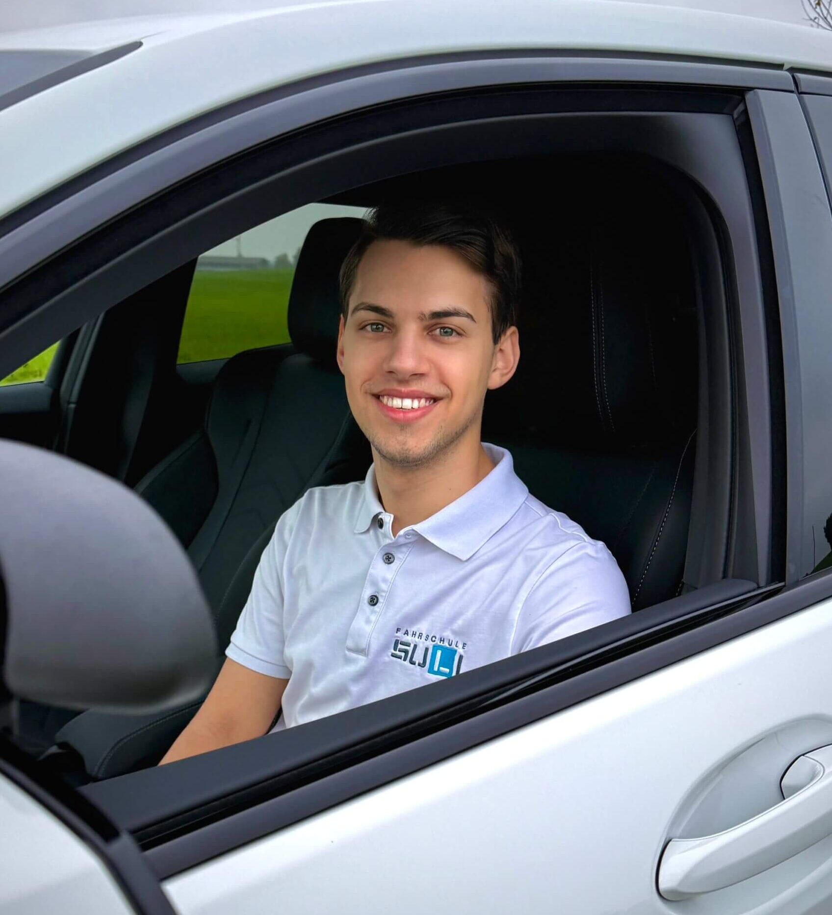 Fahrlehrer Marcel von der Fahrschule SULI in Luzern lächelt vor dem Fahrschulauto.